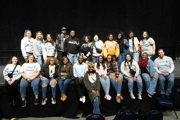 A large group of students gather along the edge of a stand and pose for a photo following a student organized university event.  